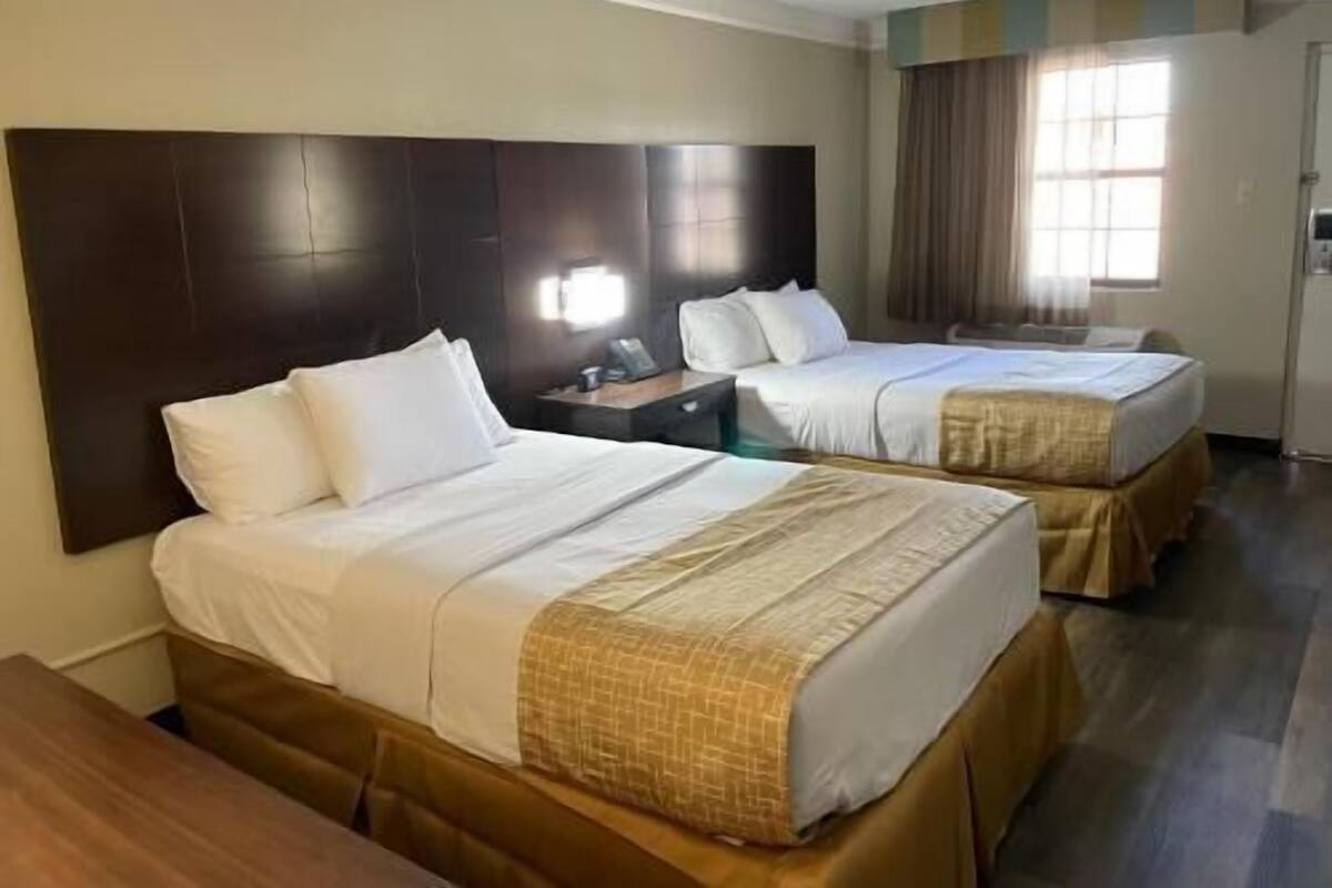 A hotel room with two beds, a large dark headboard, a nightstand, and a window with curtains.