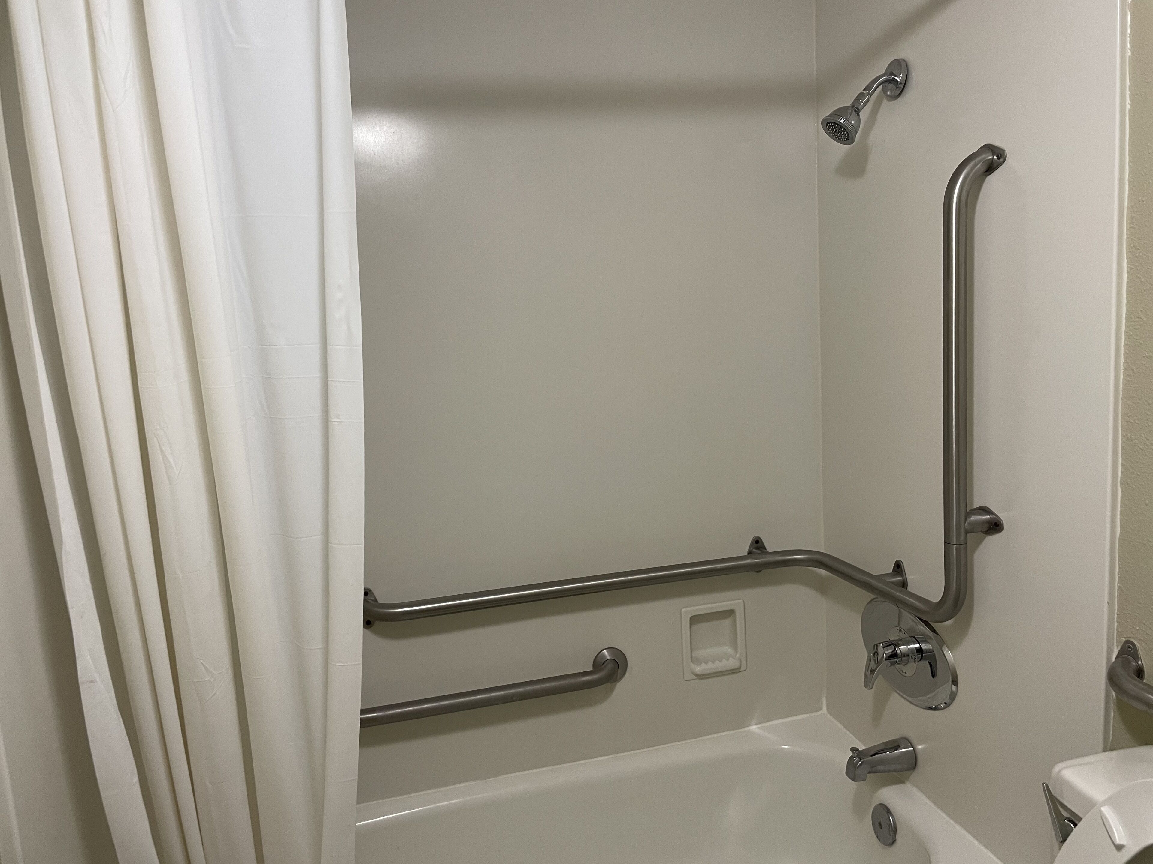 Un baño con bañera, barras de apoyo y un inodoro.