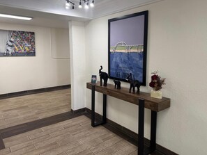 A hallway with a wooden floor, a framed artwork of a bridge, and a small shelf with figurines and a vase. - Quality Inn & Suites Tuscaloosa near University (Tuscaloosa)