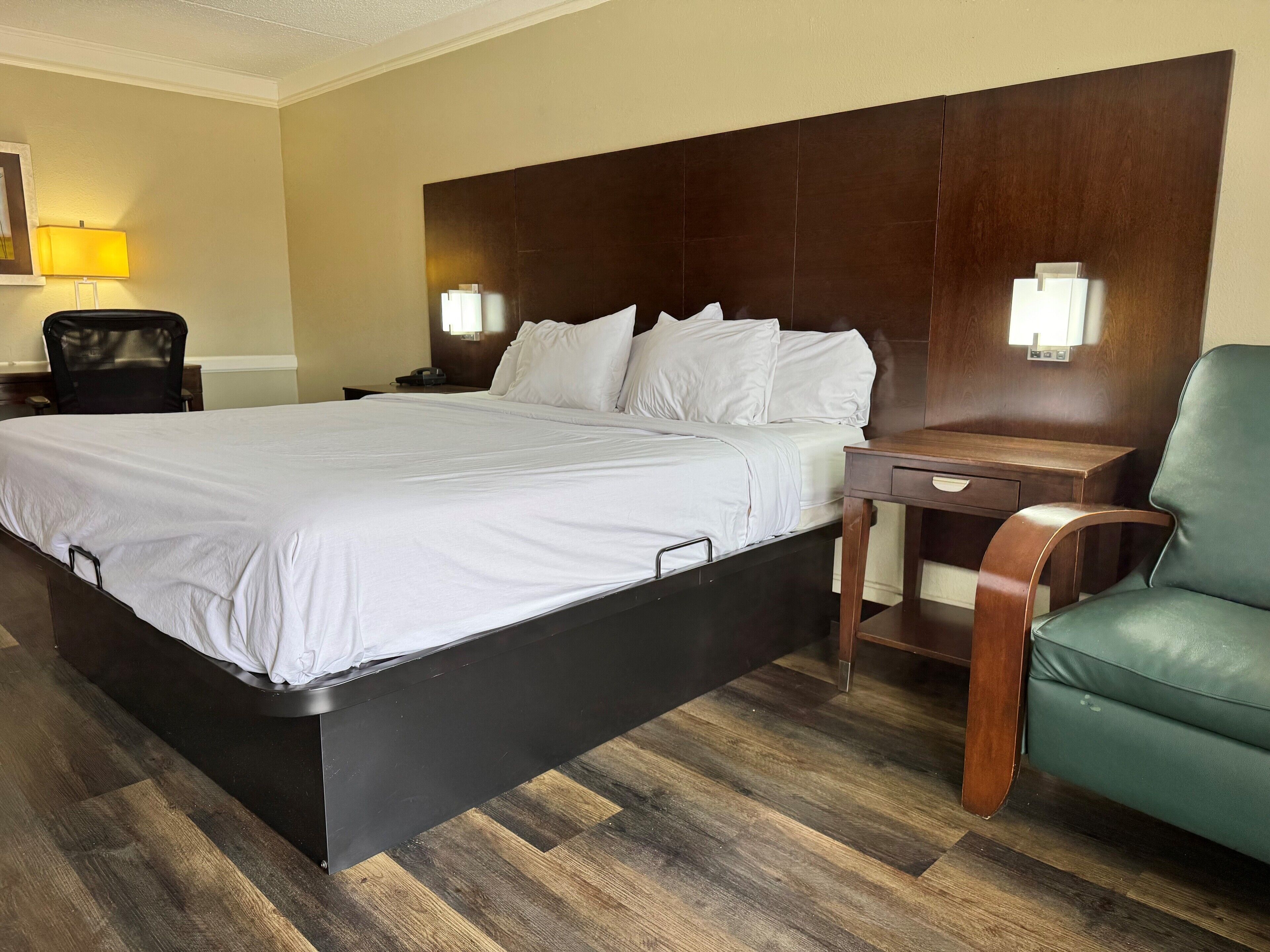A hotel room with a large bed, a wooden headboard, two bedside tables, a desk, a chair, and a lamp.