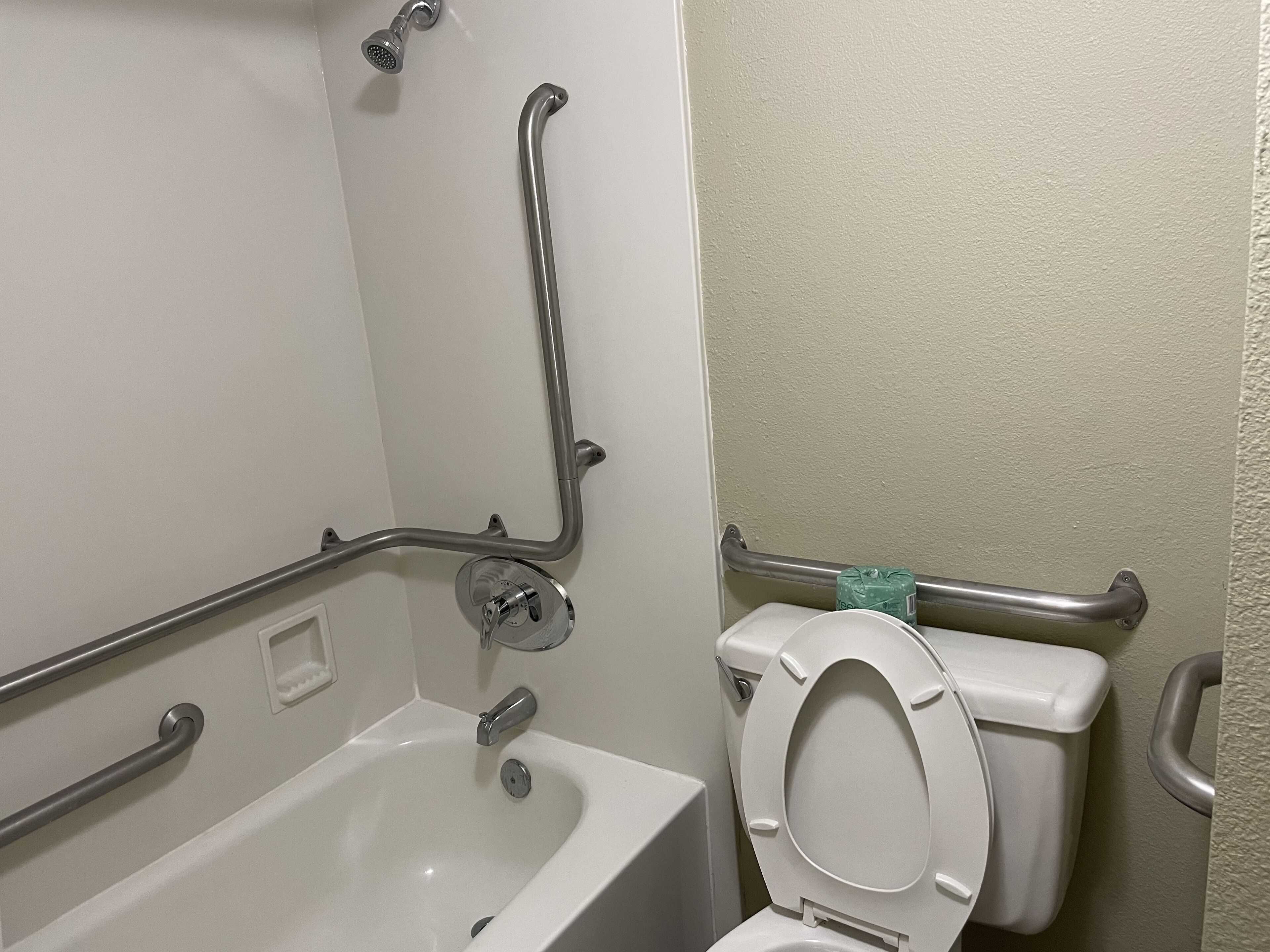 A bathroom with a bathtub, toilet, and grab bars.