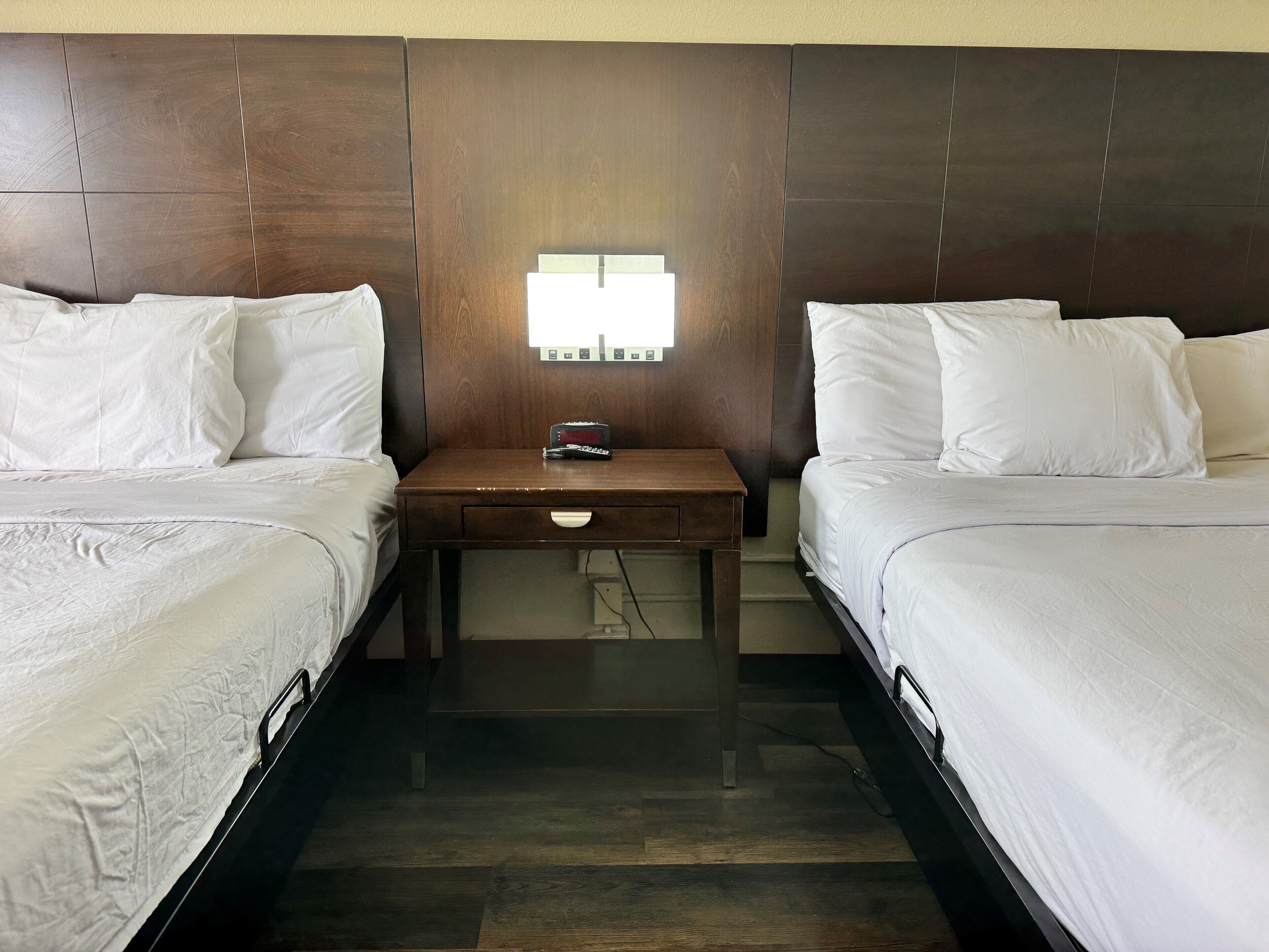 Ein Hotelzimmer mit zwei Betten, einem Nachttisch mit Lampe und einer wandmontierten Steuerung.