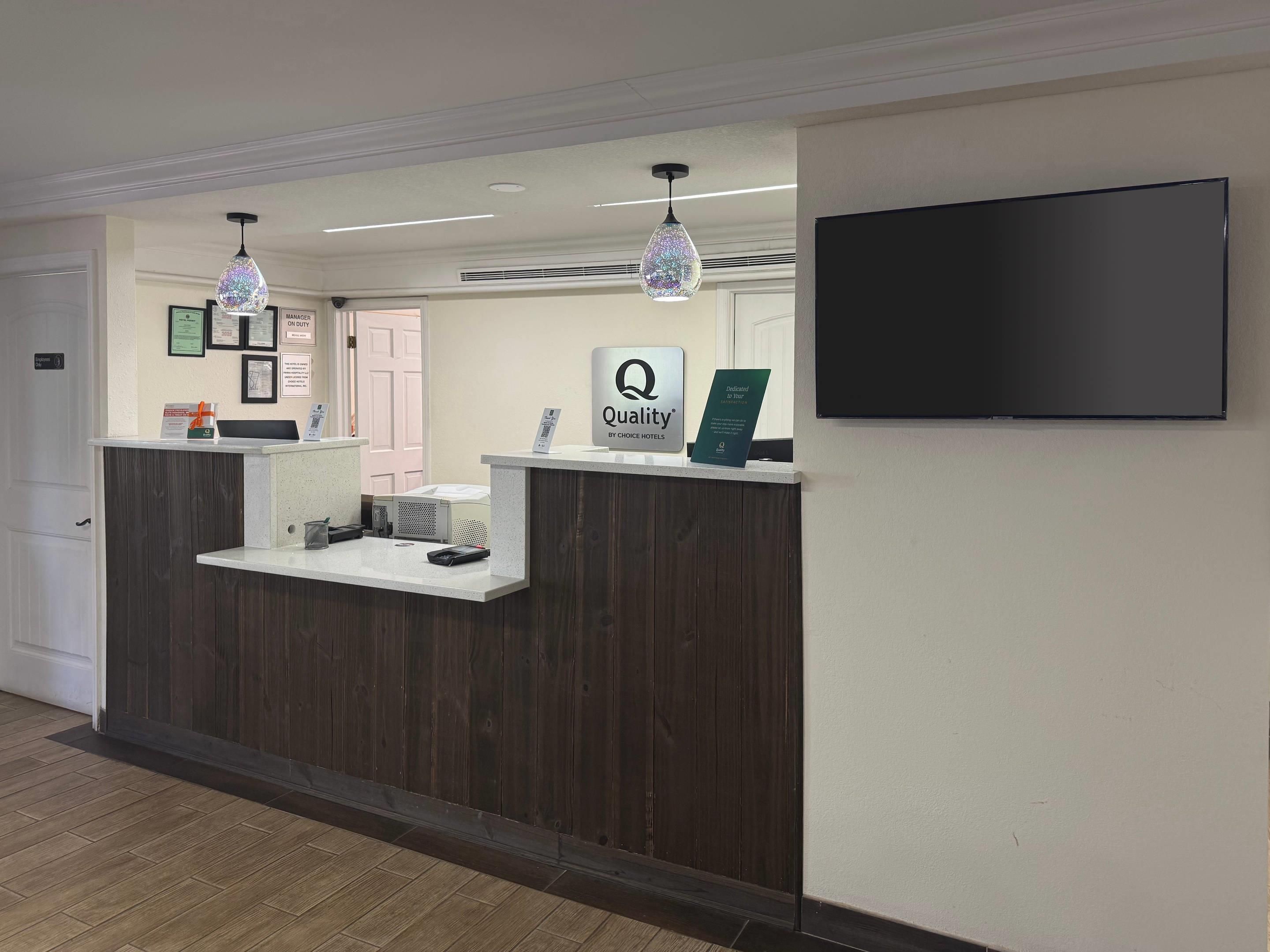 Un comptoir d’accueil d’hôtel avec une enseigne indiquant « Qualité par Choice Hotels », un téléviseur à écran plat et un comptoir d’accueil en bois.
