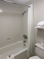 A bathroom with a bathtub, a shower, and a toilet. There is a towel rack with a towel and a roll of toilet paper on the wall.