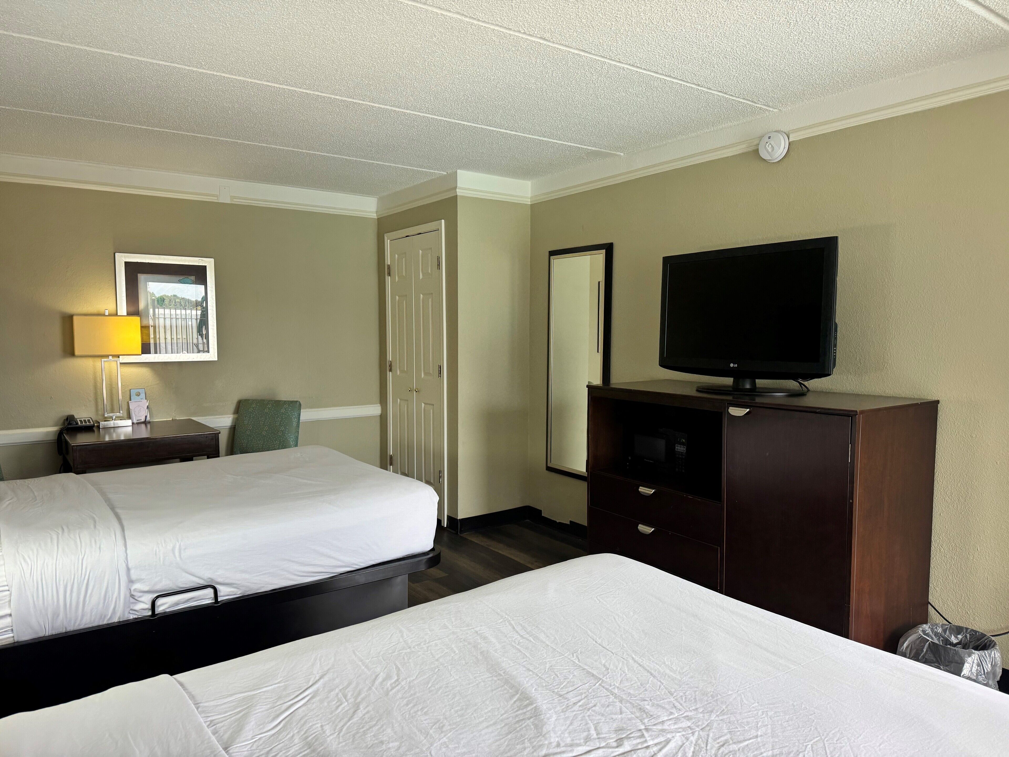 Een hotelkamer met twee bedden, een bureau met lamp, een televisie en een kledingkast.