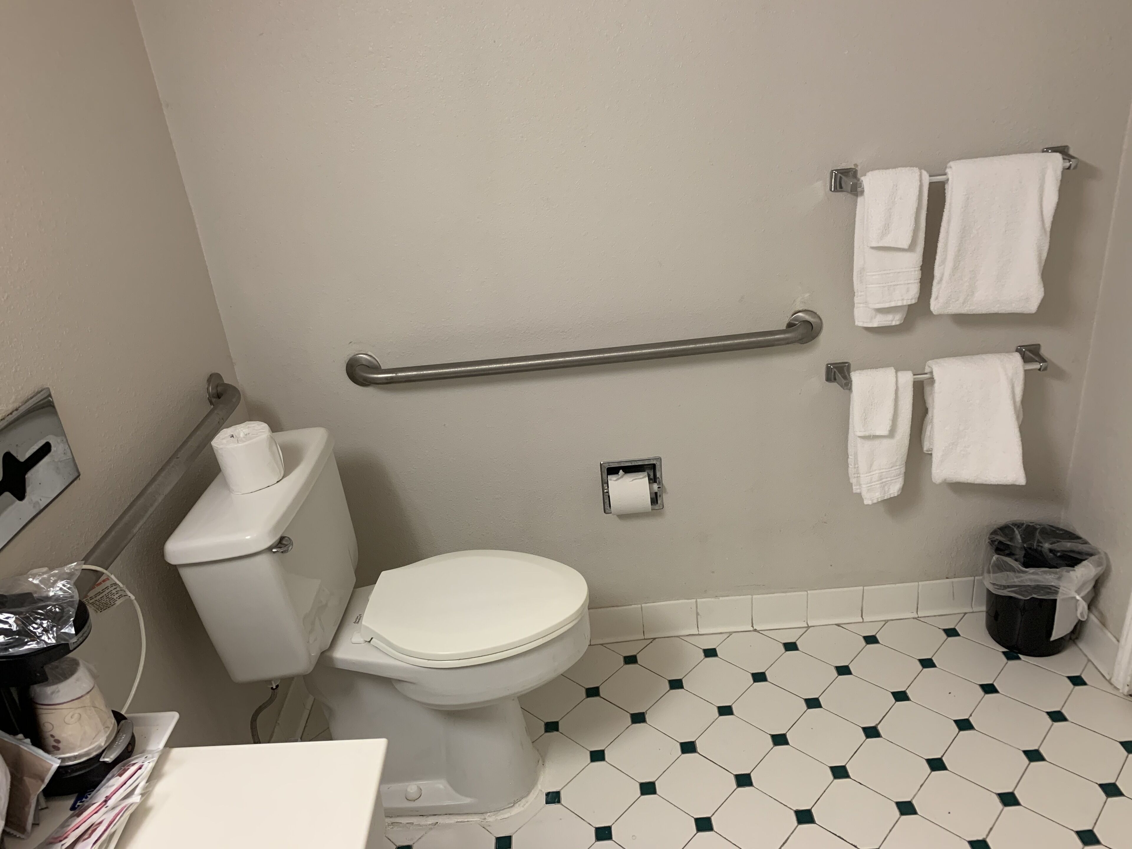 A bathroom with a toilet, handrail, and towels on a rack.