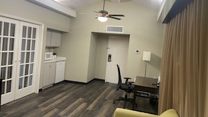 A compact kitchen with white cabinets, a microwave, and a dishwasher. There is a dining area with a table and chairs, and a ceiling fan above.