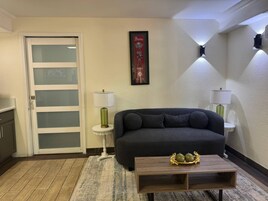 A living room with a dark sofa, a small round table with a decorative item, a white door with frosted glass panels, and two wall-mounted lamps.