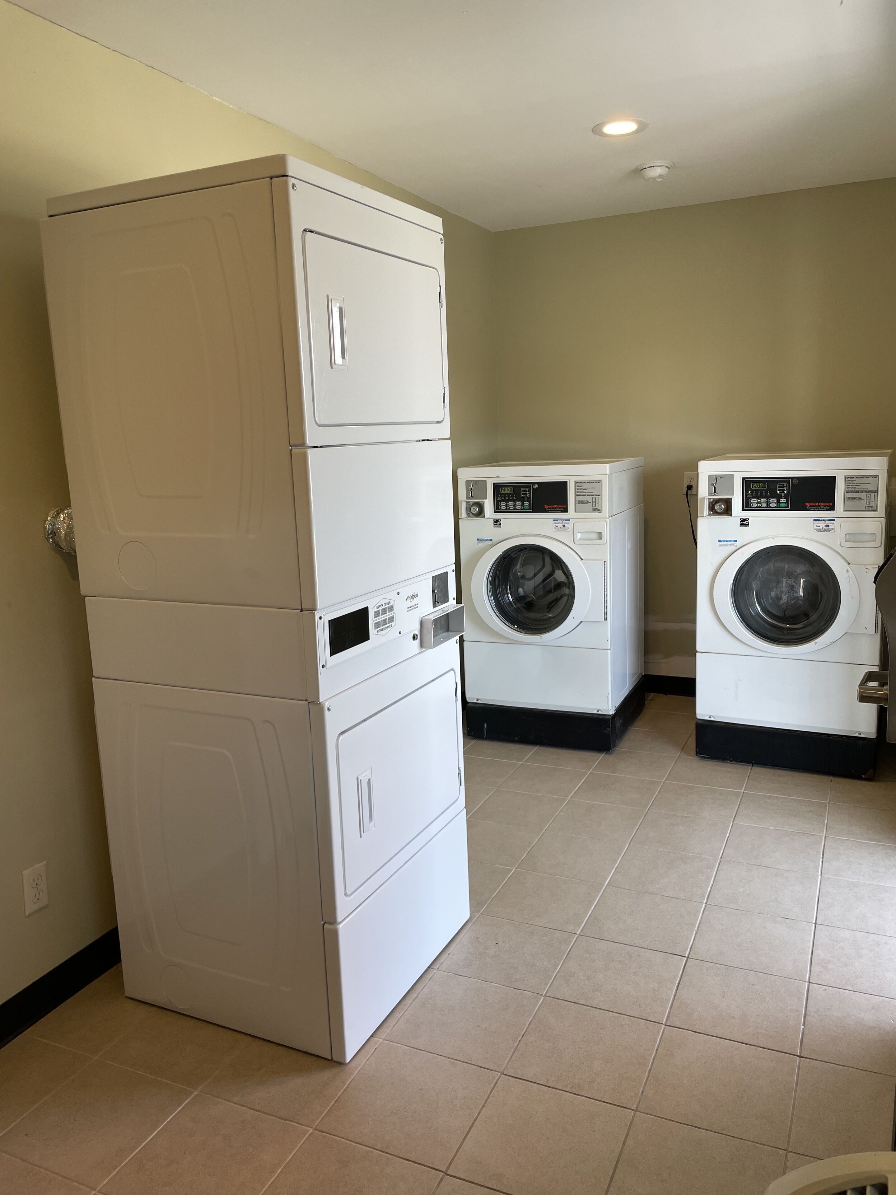 A laundry room with stacked washer and dryer units, a tiled floor, and a plain wall.