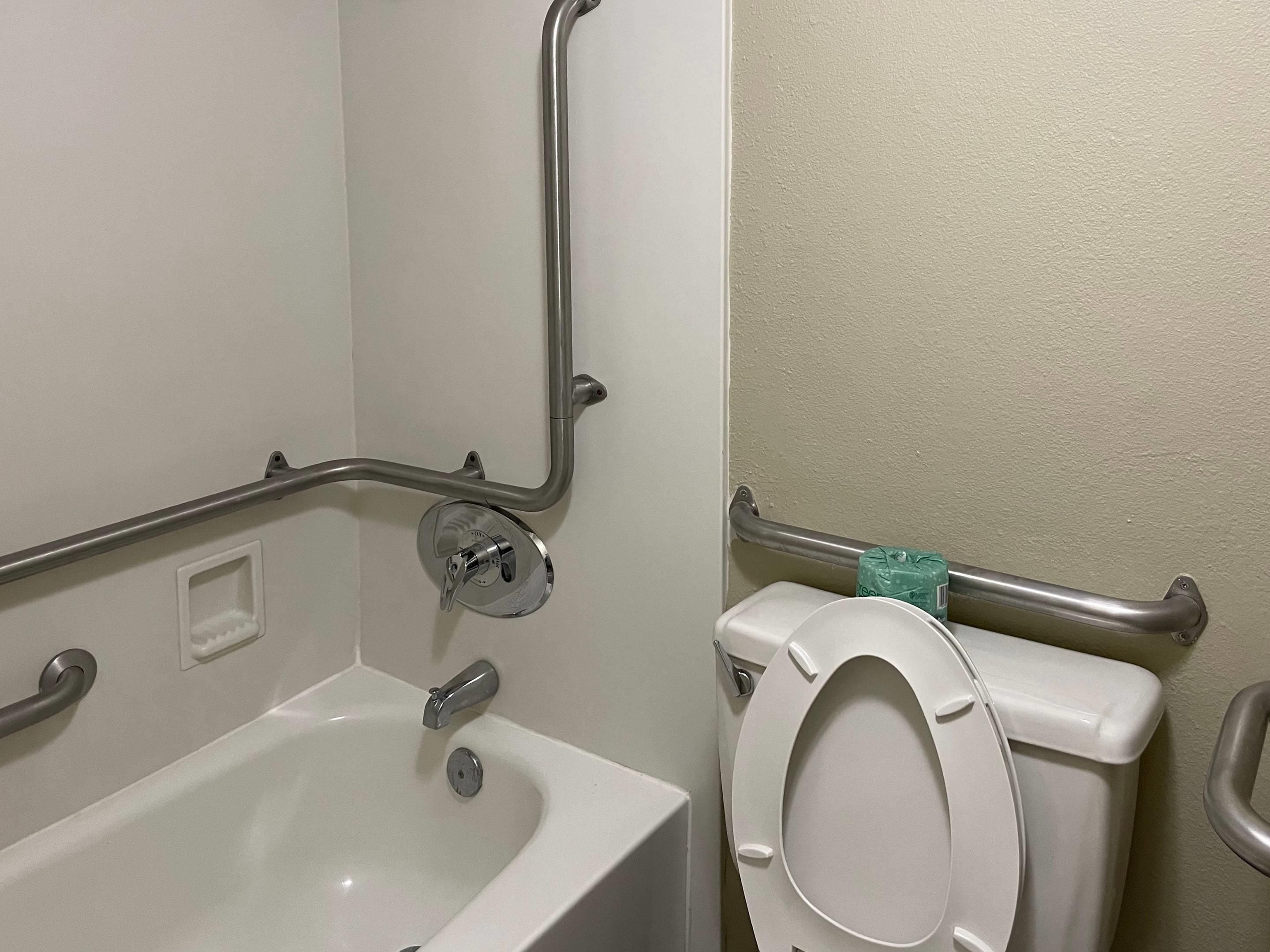 Et badeværelse med et hvidt badekar, toilet med gelænder og håndgreb.