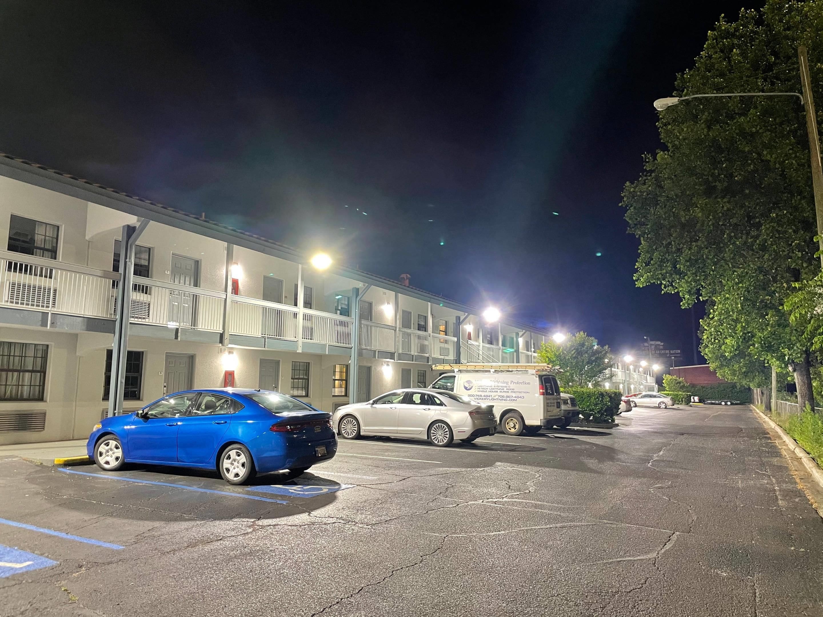 Un estacionamiento con un coche azul y una furgoneta blanca, junto a un edificio con varios pisos y balcones.