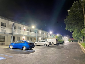 Un estacionamiento con un coche azul y una furgoneta blanca, junto a un edificio con varios pisos y balcones.