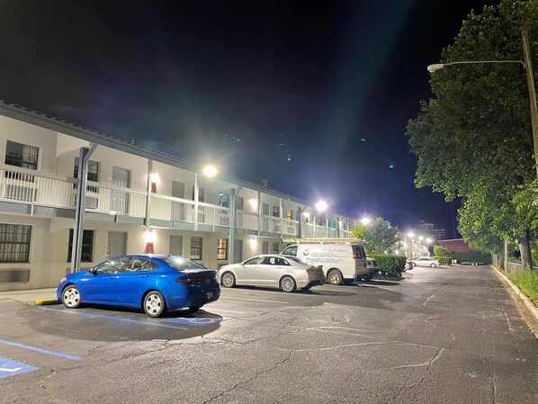 A parking lot with a blue car and a white van, adjacent to a building with multiple floors and balconies.
