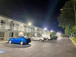 A parking lot with a blue car and a white van, adjacent to a building with multiple floors and balconies.