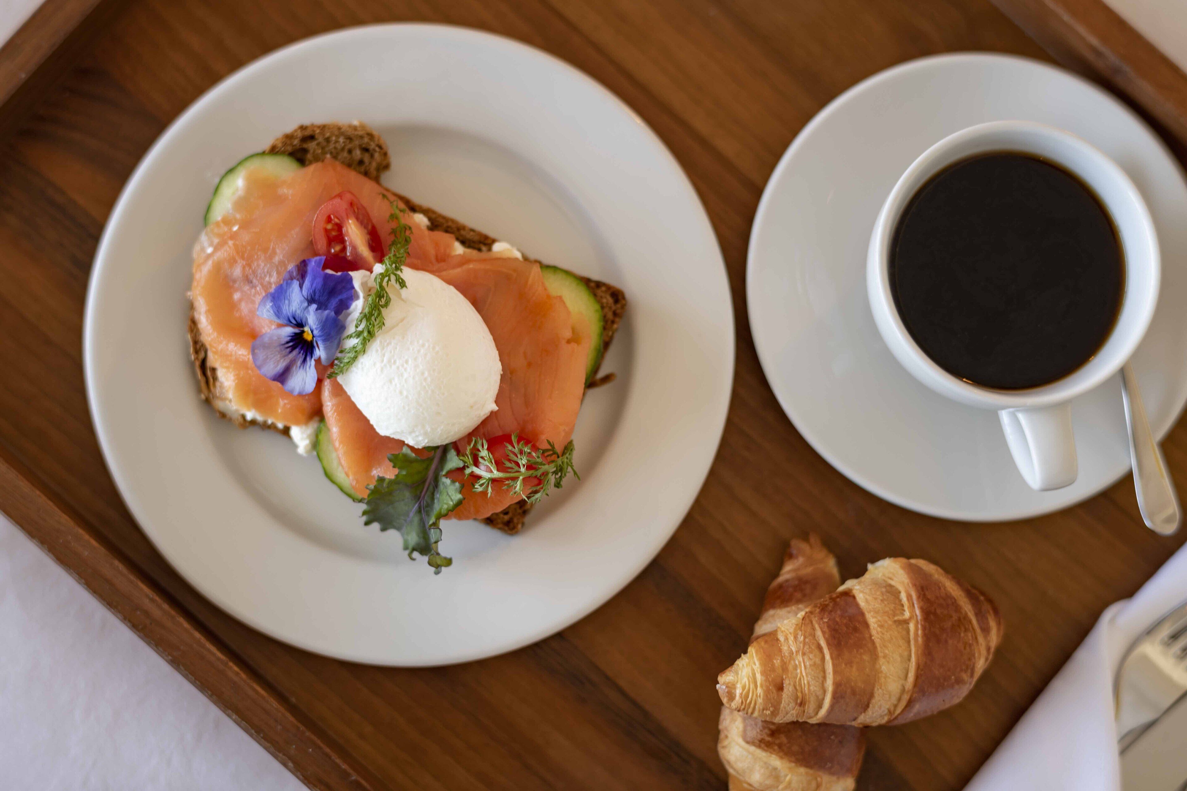Un plateau de petit-déjeuner avec une assiette de saumon fumé sur des toasts, un croissant et une tasse de café.