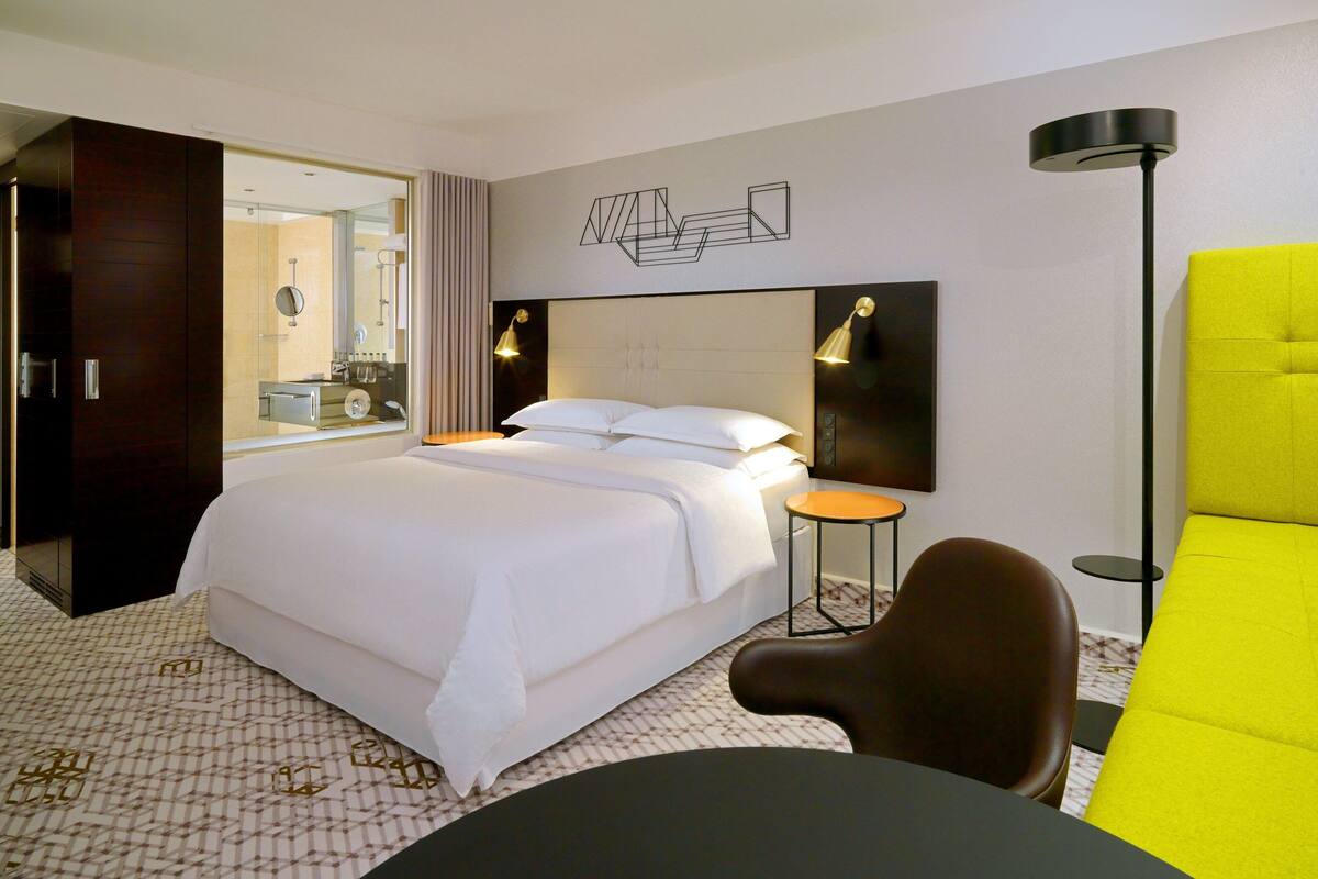 Ein Hotelzimmer mit einem großen Bett, einem Schreibtisch, einem Stuhl, einer Lampe und einem Spiegel.
