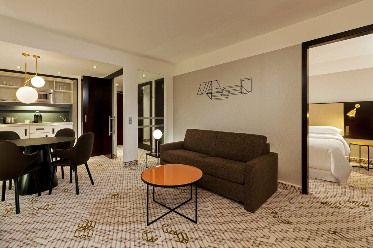 Ein modernes Hotelzimmer mit Essbereich, einer Couch, einem runden Tisch und einem Bett.