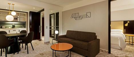 A modern hotel room with a dining area, a sofa, a round table, and a bed.