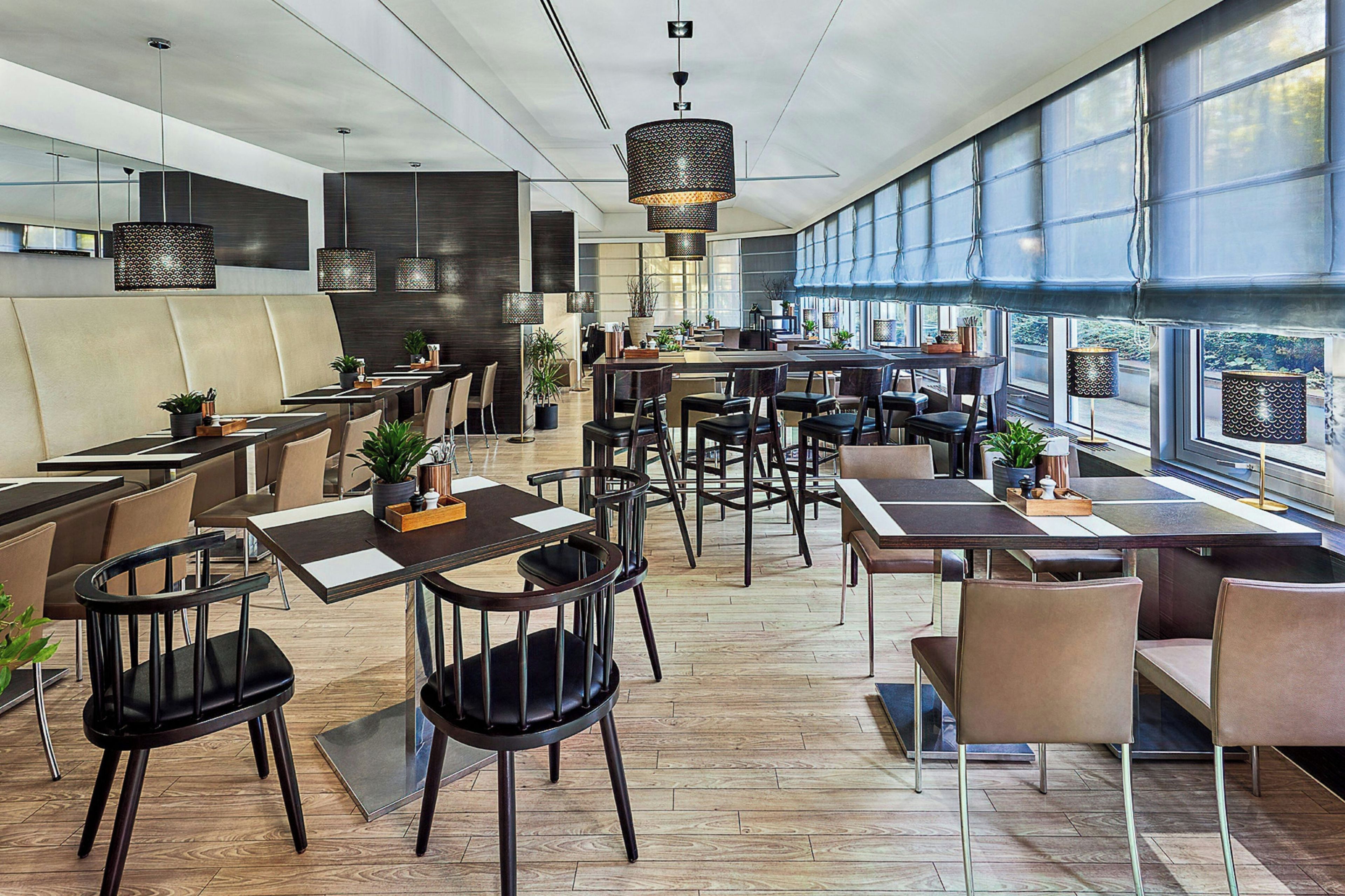 Een modern restaurantinterieur met hoge plafonds, hanglampen en grote ramen.