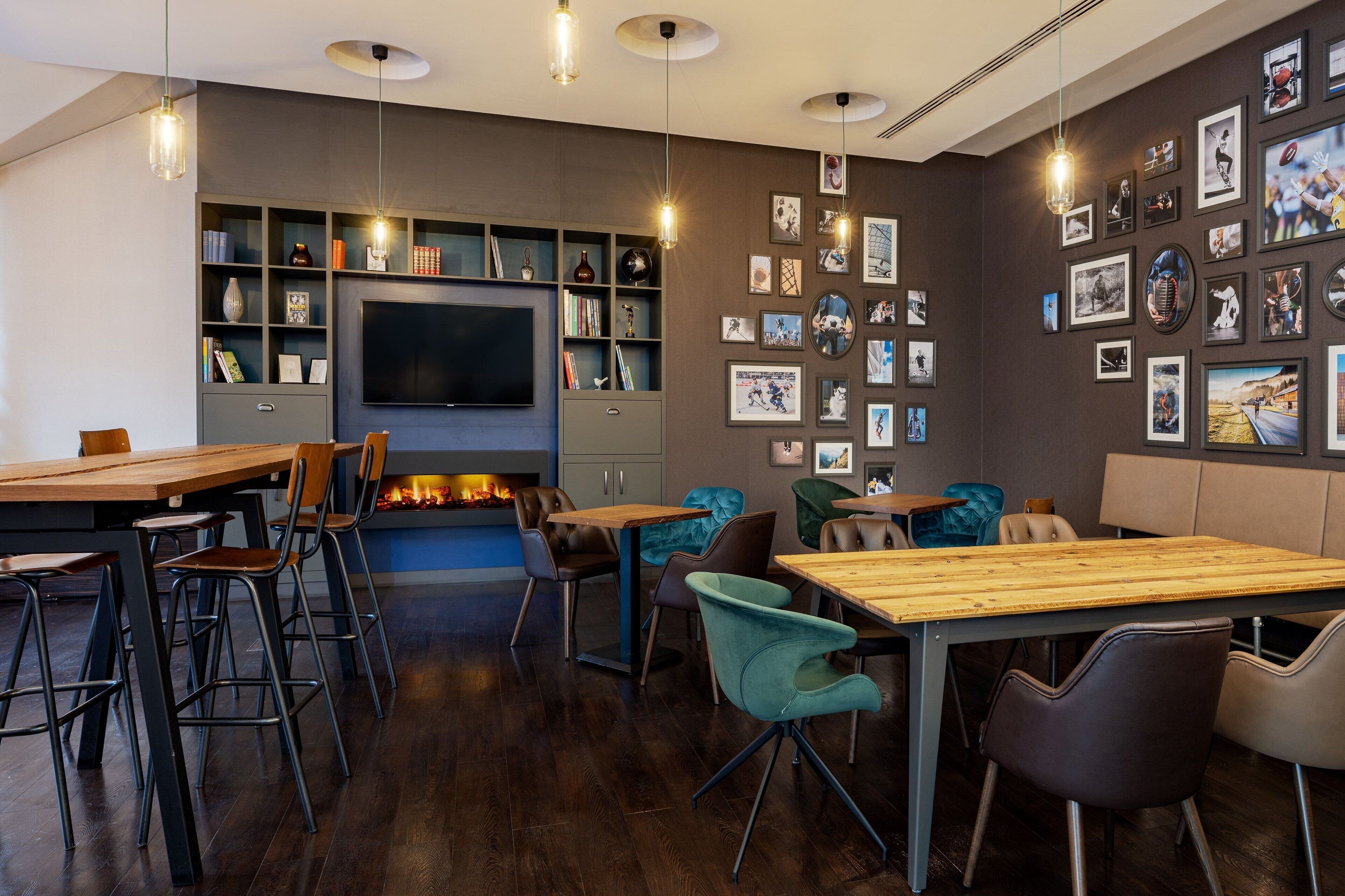 A modern lounge area with a wooden table, chairs, a fireplace, a TV, and a wall decorated with framed pictures.