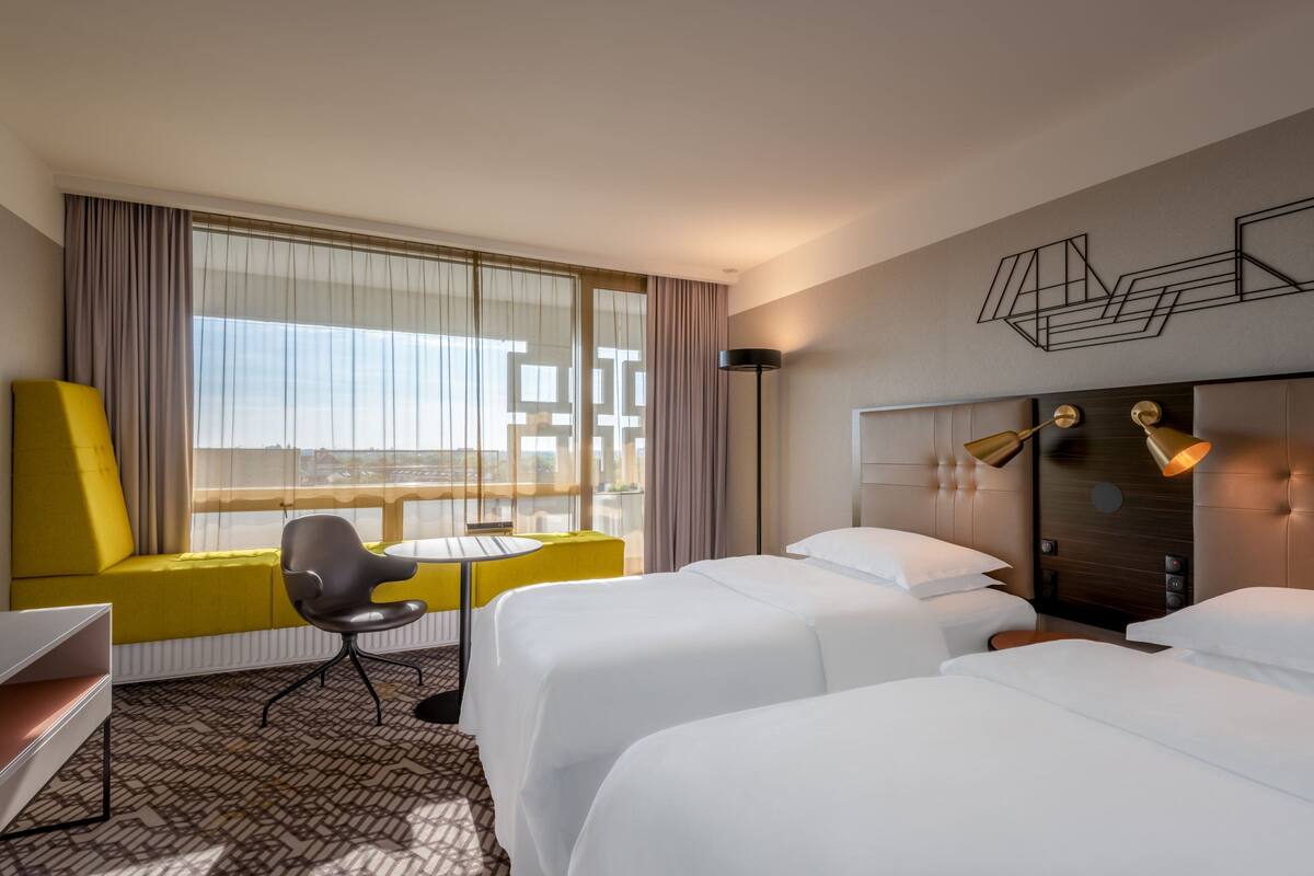 Ein Hotelzimmer mit zwei Betten, einem gelben Sofa, einem kleinen Tisch und einem Stuhl.