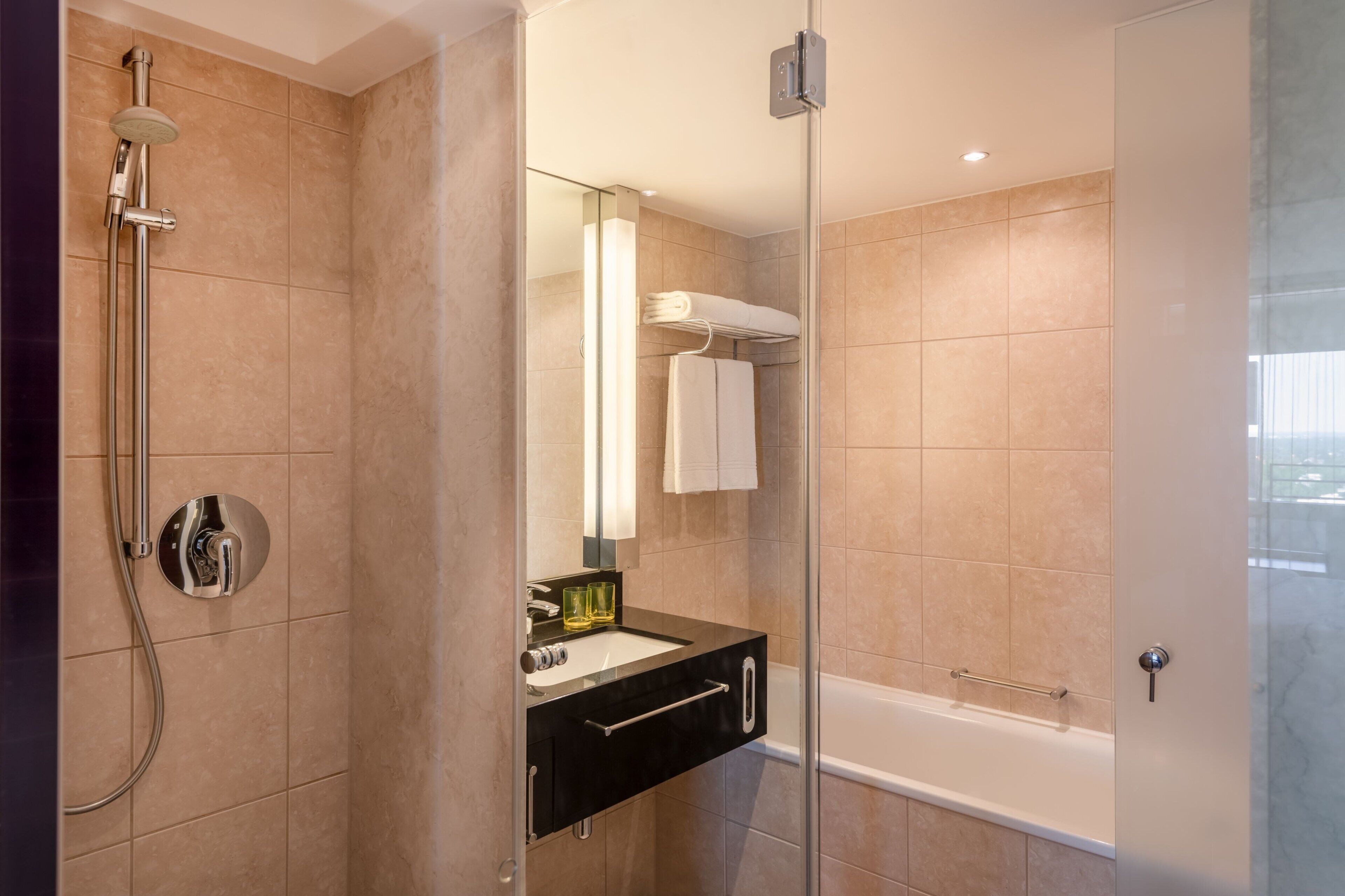 Un baño moderno con ducha envuelta en vidrio, un tocador negro con lavamanos y una bañera blanca.