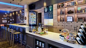 Een bar met krukken, een koffiemachine en een presentatie van gebak en drankjes.