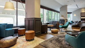 Een moderne hotellobby met zithoeken, grote ramen en een open haard.