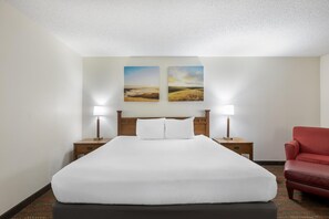 A hotel room with a large bed, two bedside tables with lamps, a red chair, and two landscape paintings on the wall. - Best Western La Grande Hacienda (Cherokee)