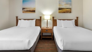 A hotel room with two beds, a nightstand with a lamp, and two landscape paintings on the wall.