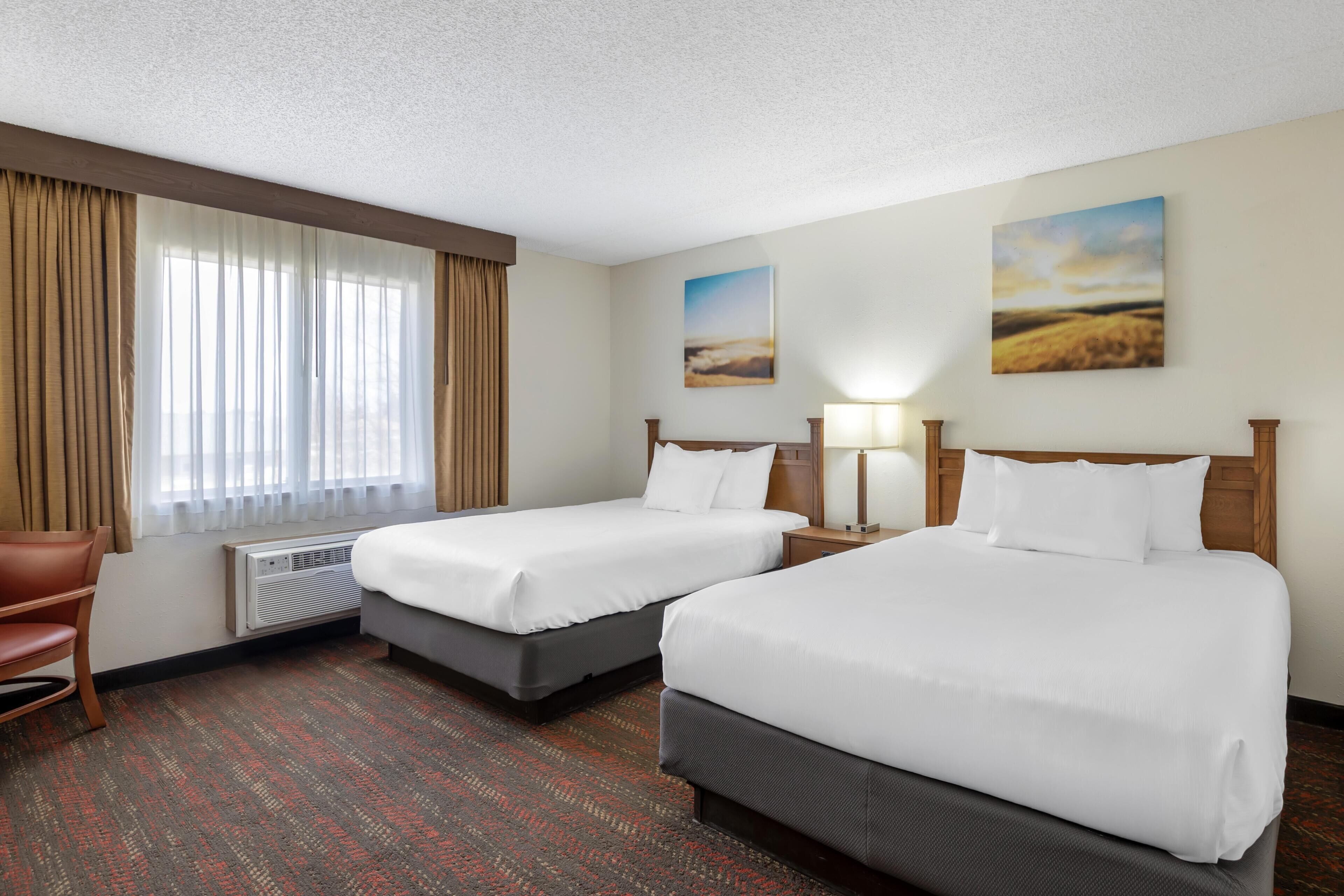 A hotel room with two beds, a chair, a radiator, and two paintings on the wall.