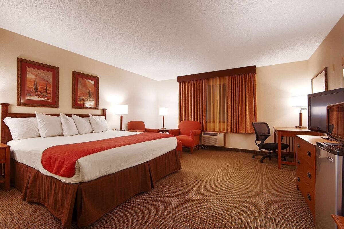 Habitación de hotel con una cama grande, dos lámparas de noche, un escritorio con televisor, una silla y dos cuadros en la pared.