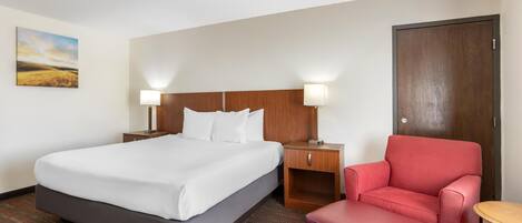 A hotel room with a bed, two bedside tables with lamps, a red chair, a wooden door, and a painting on the wall.