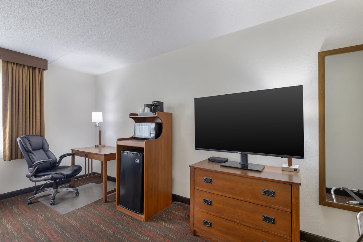 Habitación de hotel con televisión de pantalla plana, escritorio con microondas, silla, refrigerador y cómoda.