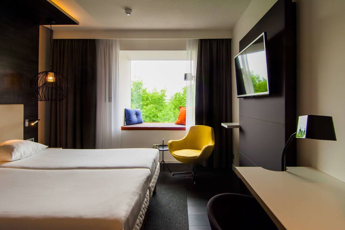 Une chambre d’hôtel équipée d’un lit, d’un bureau, d’une chaise, d’une télévision et d’une fenêtre donnant sur un paysage verdoyant.