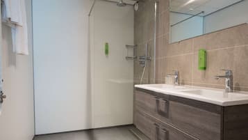 A modern bathroom with a large mirror, dual sinks, and a walk-in shower.