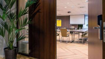 A conference room with a large screen, wooden flooring, and a potted plant.