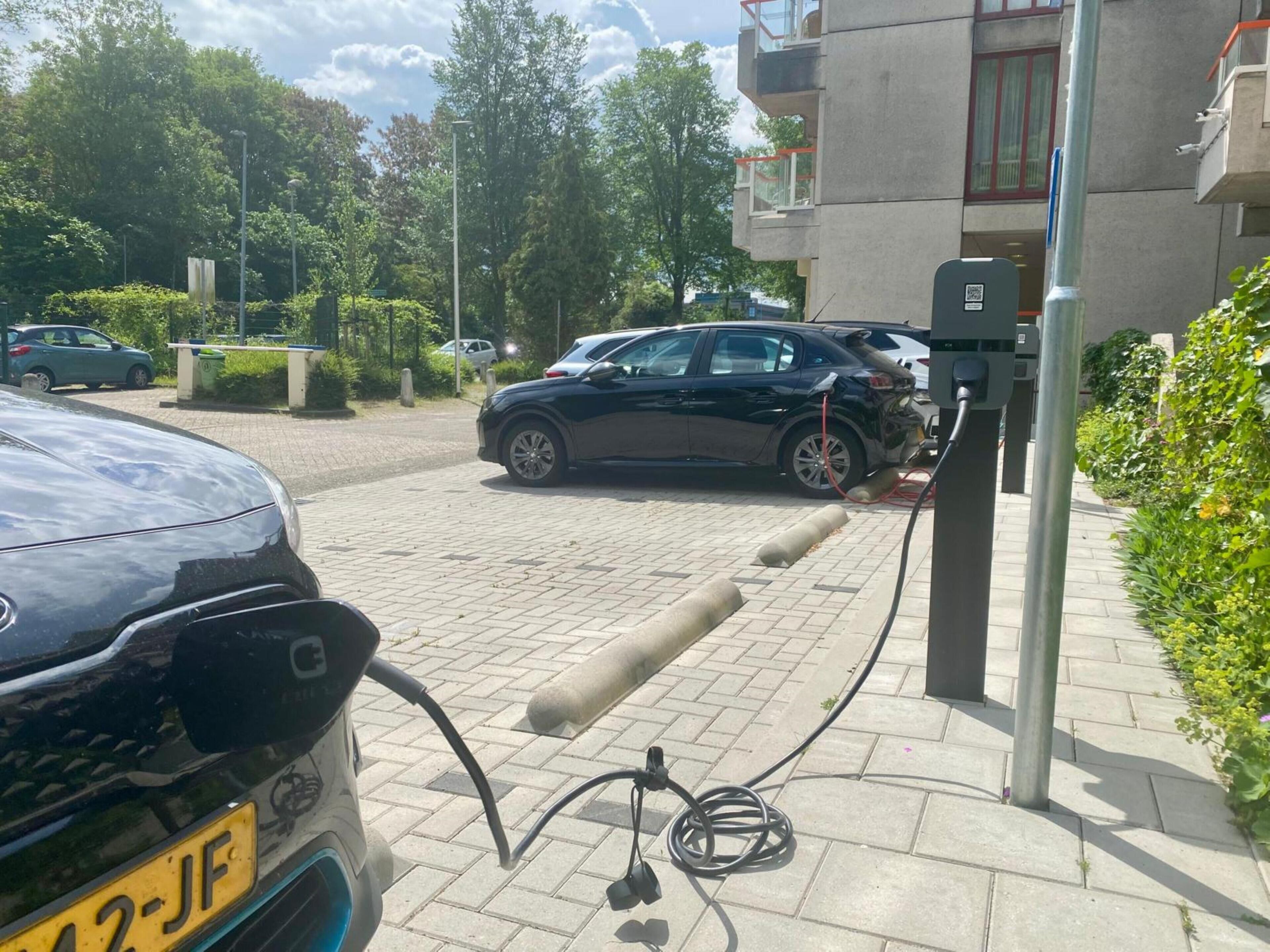 Un área de estacionamiento con estaciones de carga para vehículos eléctricos, un camino pavimentado y zonas verdes.