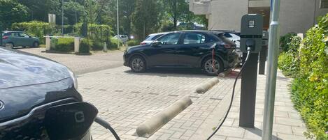 Un área de estacionamiento con estaciones de carga para vehículos eléctricos, un camino pavimentado y zonas verdes.