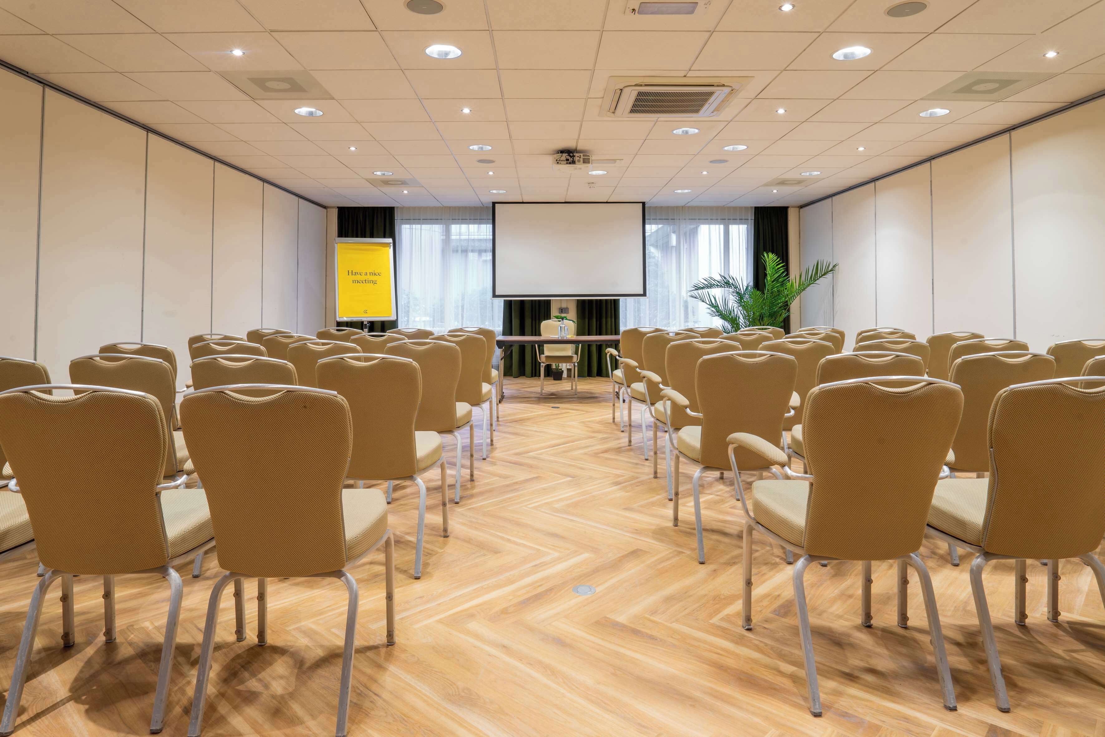 Een vergaderzaal met rijen stoelen, een projectiescherm en een presentatiescherm.