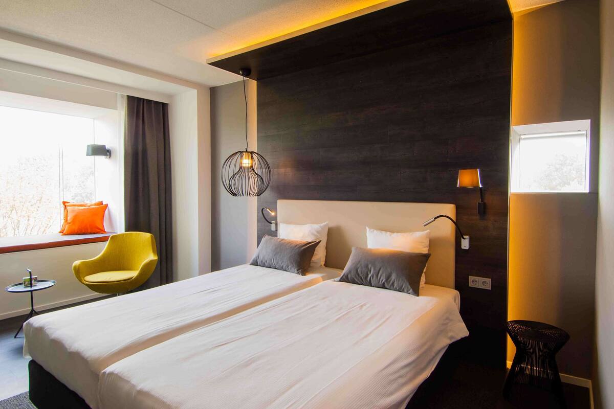 Une chambre d’hôtel avec un grand lit, deux tables de chevet, une chaise et une fenêtre avec des rideaux.