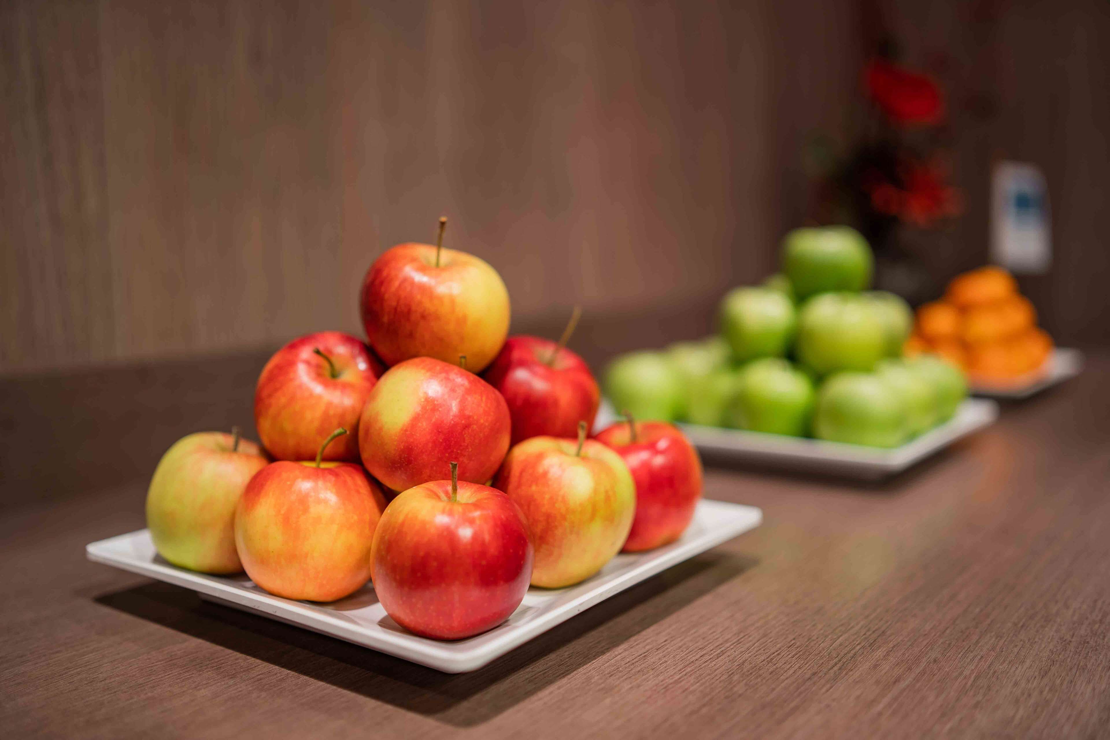A wooden table with two white plates of apples, one plate with red and yellow apples and another with green apples.