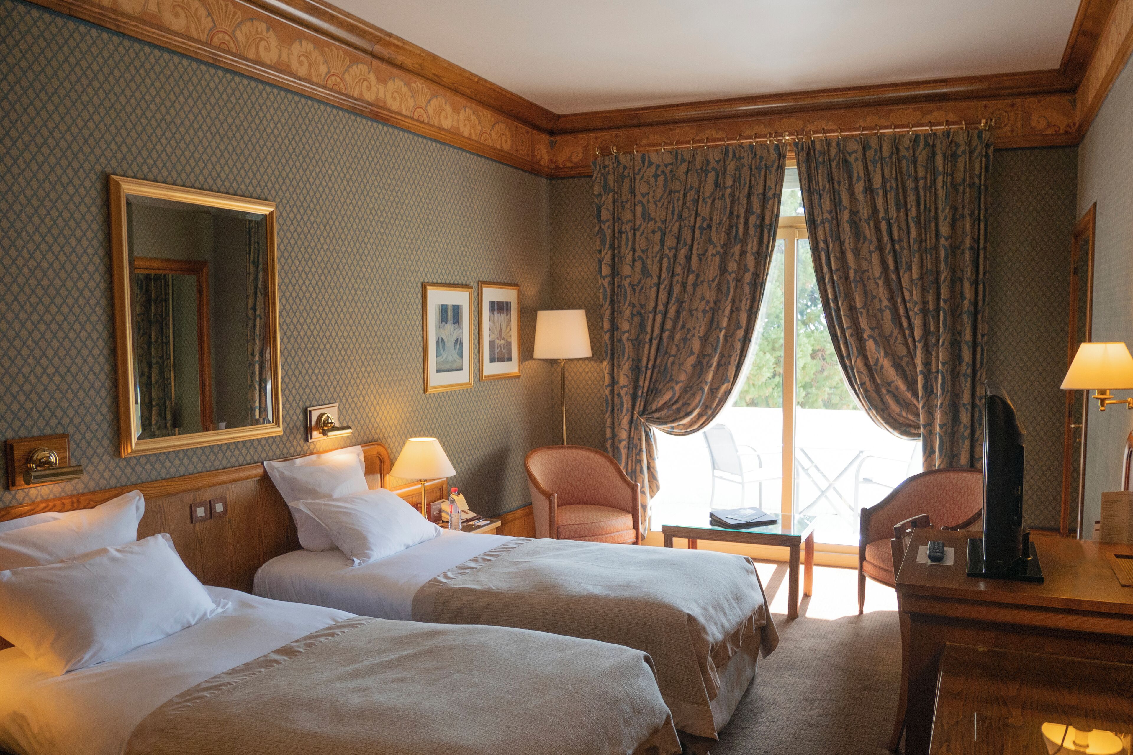 Habitación de hotel con dos camas, un escritorio, una silla, un televisor y una ventana con cortinas.