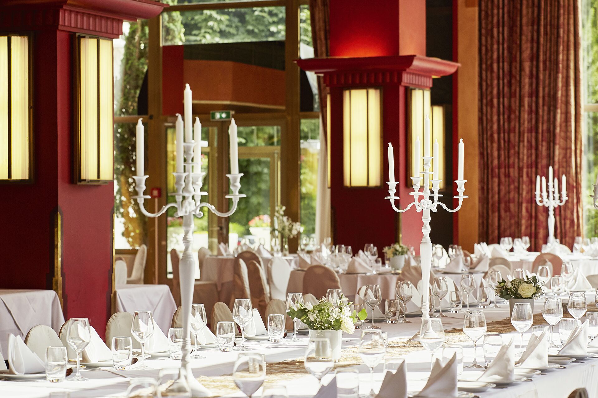 A formal dining setting with white table settings, candelabras, and a view of greenery outside.