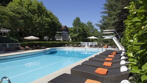 A swimming pool with lounge chairs and umbrellas, surrounded by trees and a building.