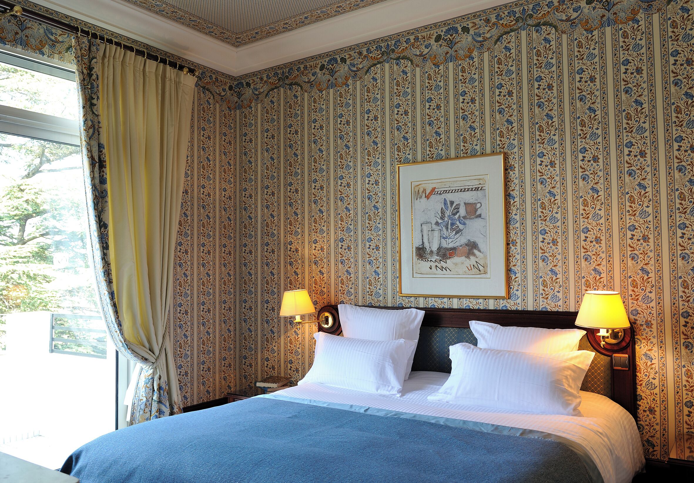 Ein Hotelzimmer mit einem großen Bett, zwei Nachttischlampen und einem blumigen Wandmuster.