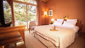 Une chambre d’hôtel avec un grand lit, un bureau avec une télévision, une chaise et une vue sur les arbres par la fenêtre.
