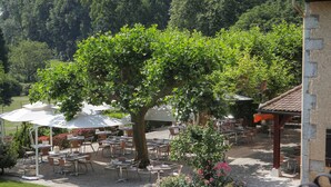 An outdoor patio with tables and chairs, surrounded by greenery and trees.