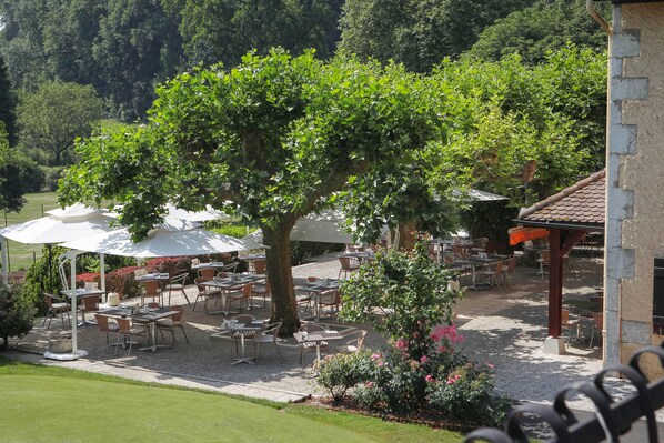 An outdoor patio with tables and chairs, surrounded by greenery and trees.