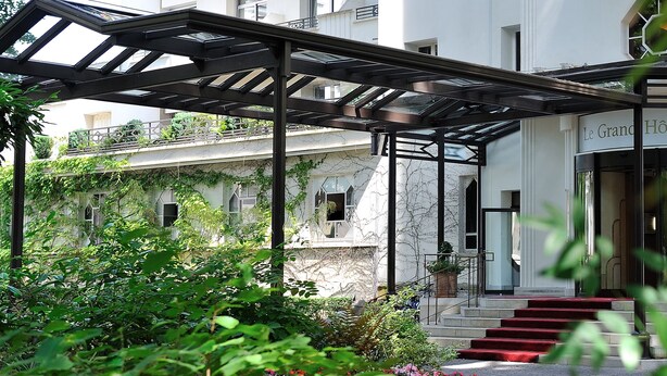 A hotel entrance with a covered outdoor area, steps leading up to the entrance, and a sign reading "Le Grand Hôtel".